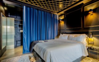 Apartamento Shibari en Madrid Río con cortinas de terciopelo, iluminación cálida y cama central sobre paredes en negro.